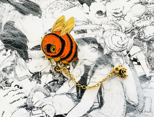 An enamel pin shaped like a bee with orange and black colors and a spooky spider attached to it